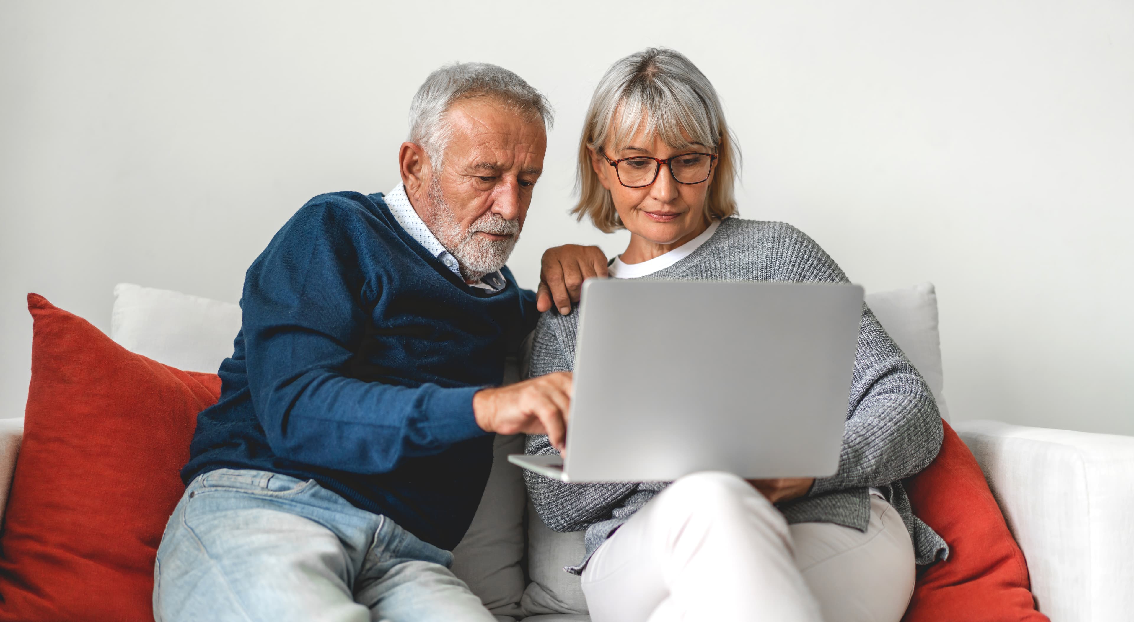 An older couple on a sofa, looking at a laptop together